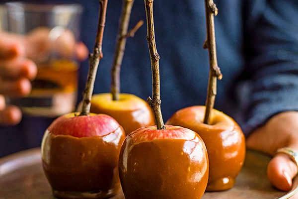 A hand holding a golden tray of apples dipped in bourbon butterscotch