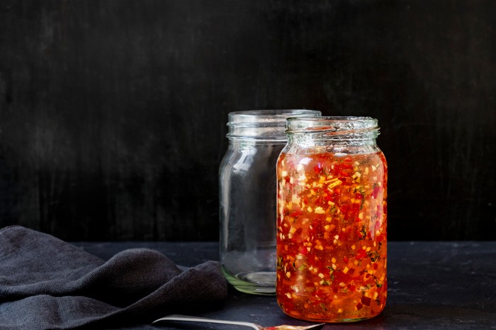 A dark black background with two glass jars, one filled with a red jelly