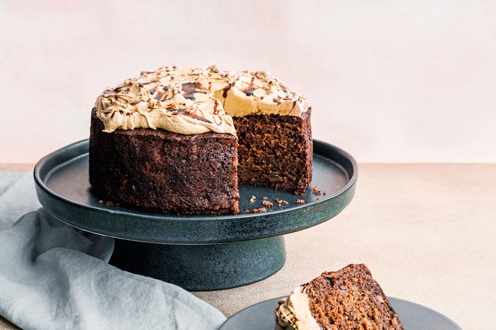 A cake stand topped with a dark sponge cake with a light brown soft cheese frosting