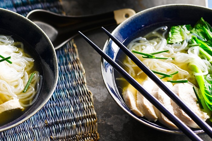 Two bowls of zero noodles in a chicken broth with a pair of chopsticks on top