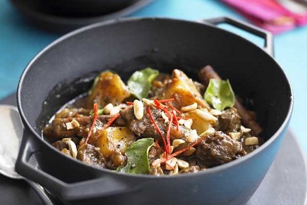 Bowl of beef massaman curry on a plate with a spoon