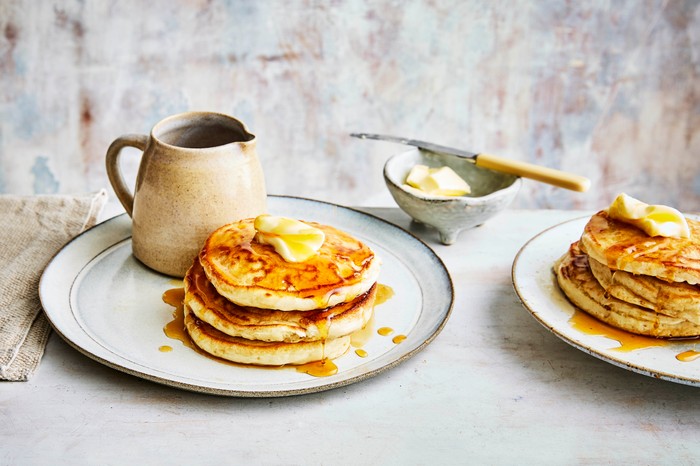 American pancakes in a stack next to a jug of maple syrup