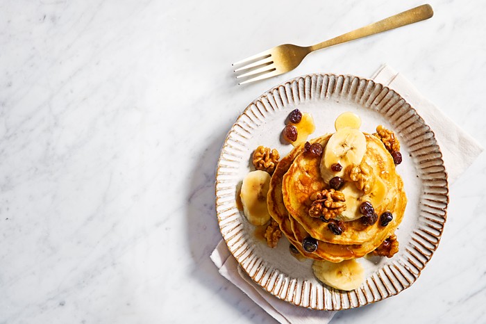 A stack of pancakes with raisins, walnuts and banana