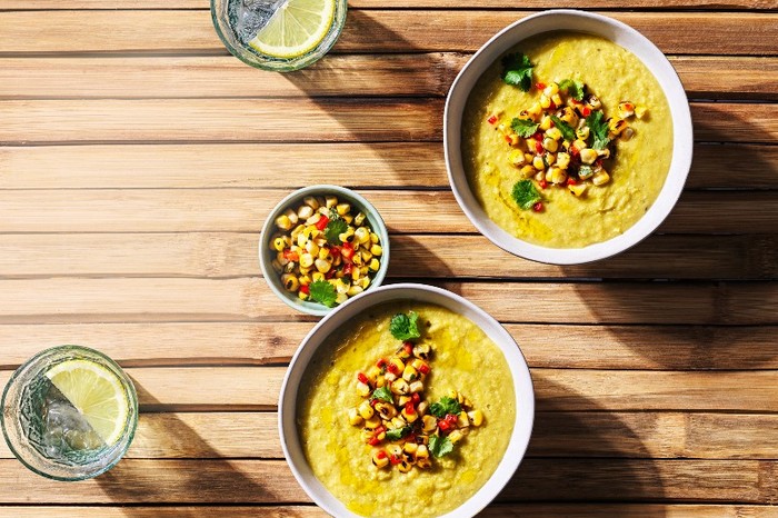 Two bowls of yellow soup on a wooden table topped with salsa