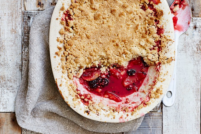 Apple and blackberry crumble in a white oval baking dish with a portion taken out