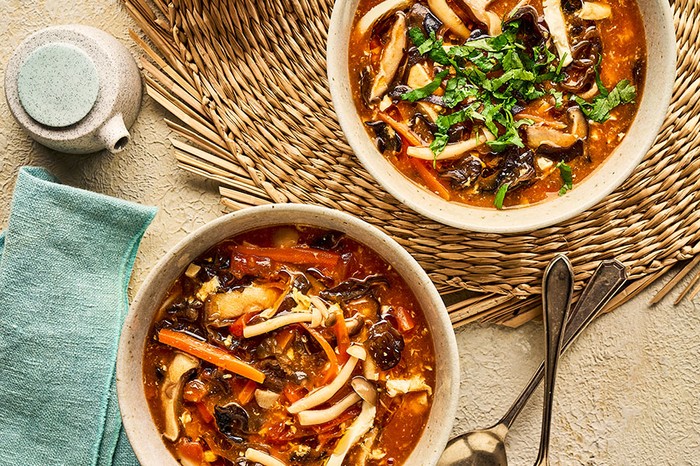 Two bowls of mushroom, tofu and carrot hot and sour soup topped with coriander