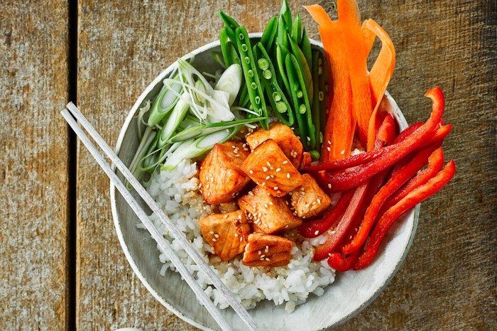 Bowl of sushi rice topped with raw salmon and vegetables