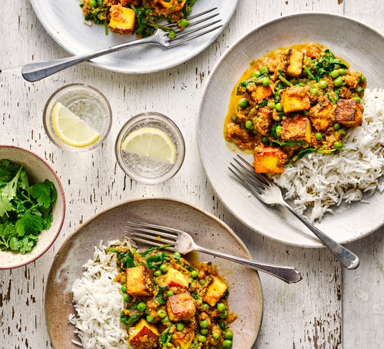 Two plates of paneer curry with rice, with forks and two glasses of water with lemon wedges