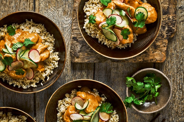 Three bowls filled with chicken, rice and salad, placed on a wooden table