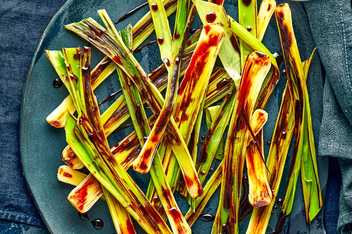 A dark blue plate topped with small green leeks drizzled with a red balsamic dressing