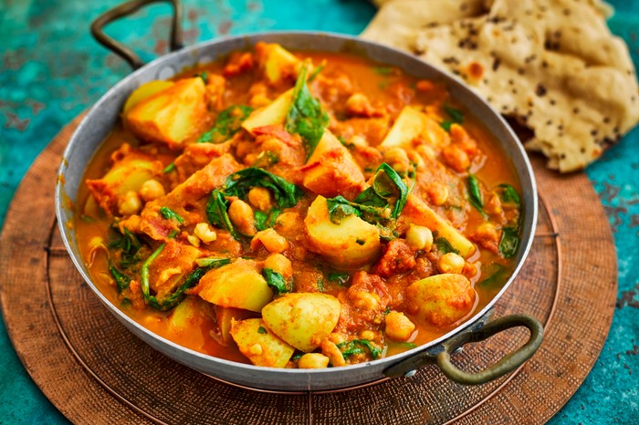 Spinach, chickpea and potato curry in a skillet with some naan breads