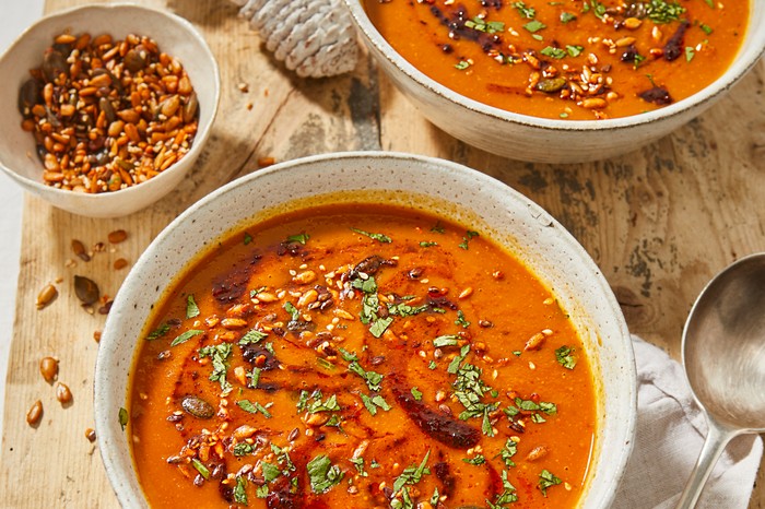 Two bowls filled with orange soup topped with seeds