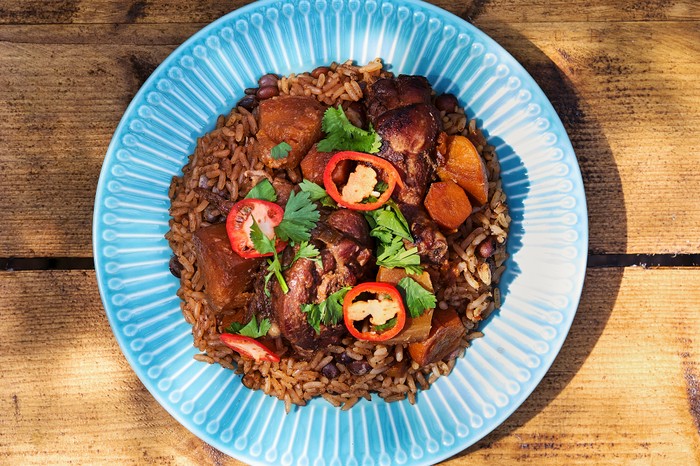 A wooden table with a blue plate, topped with rice, chicken and sliced red chilli