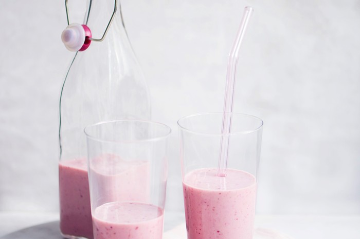 A glass bottle of smoothie with two glasses in front of it