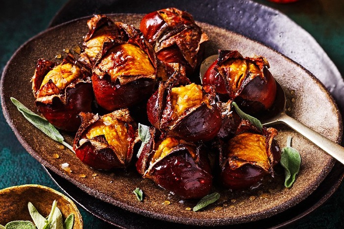 A brown bowl of roasted chestnuts with a small pot of sage leaves