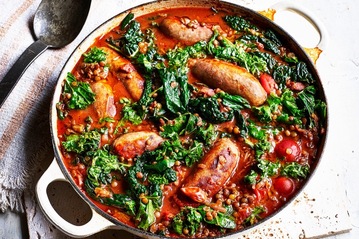 Pot of sausage and lentil casserole on a tea towel next to a spoon