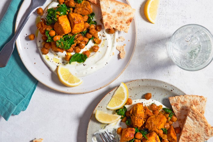 Two plates of spiced chicken with lemon wedges on the side