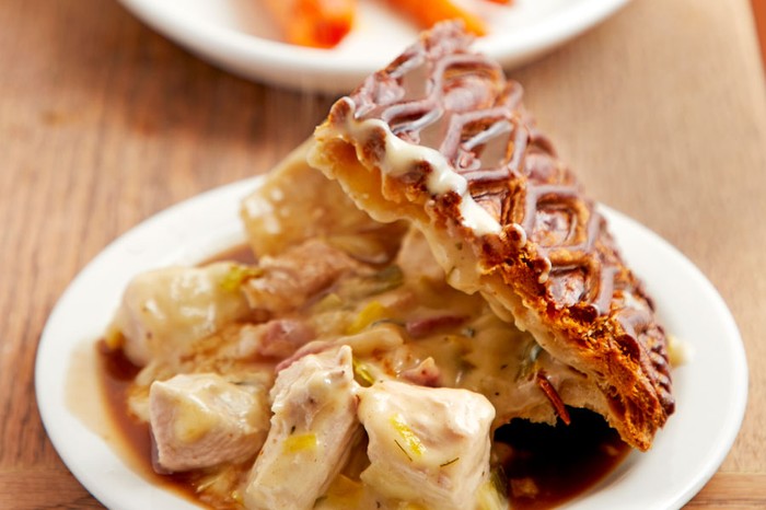 Turkey, leek and bacon pie on a plate covered in gravy with carrots on plate behind